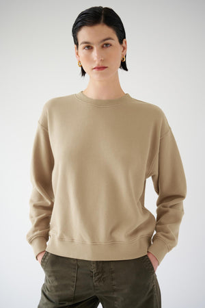 Woman posing in a plain beige Velvet by Jenny Graham Ynez sweatshirt and green pants against a light background.