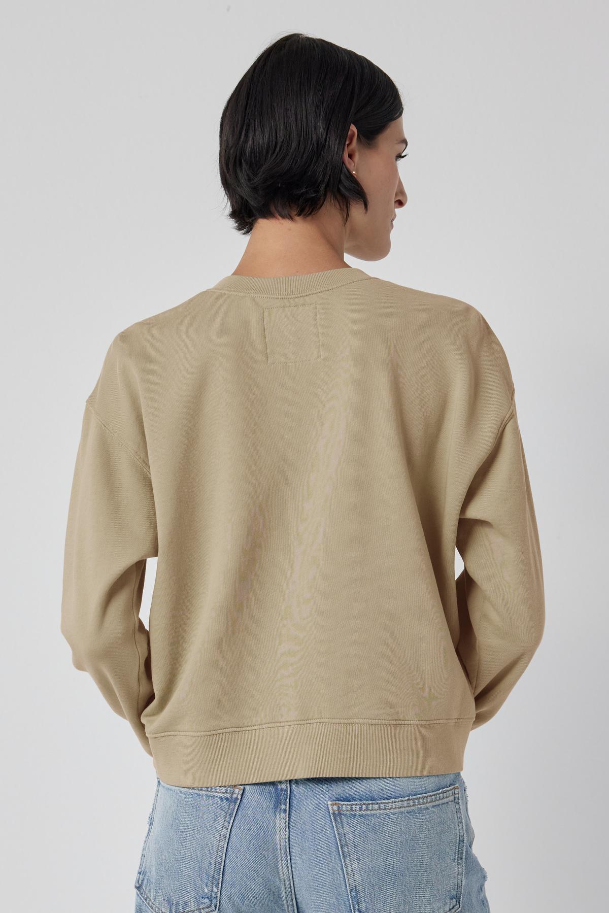 A woman seen from behind wearing a beige Ynez Sweatshirt by Velvet by Jenny Graham and blue jeans.-36463630844097