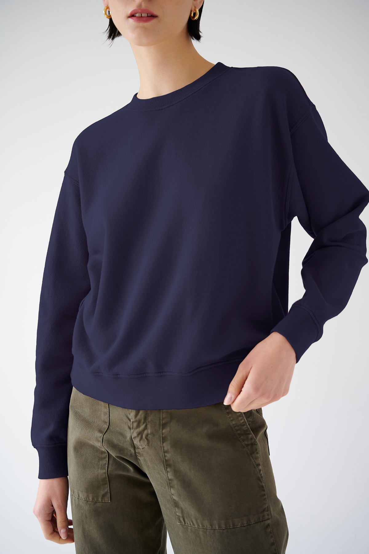   A woman in a dark blue Velvet by Jenny Graham YNEZ SWEATSHIRT made from organic cotton and olive green cargo pants against a light background. Only her torso is visible. 