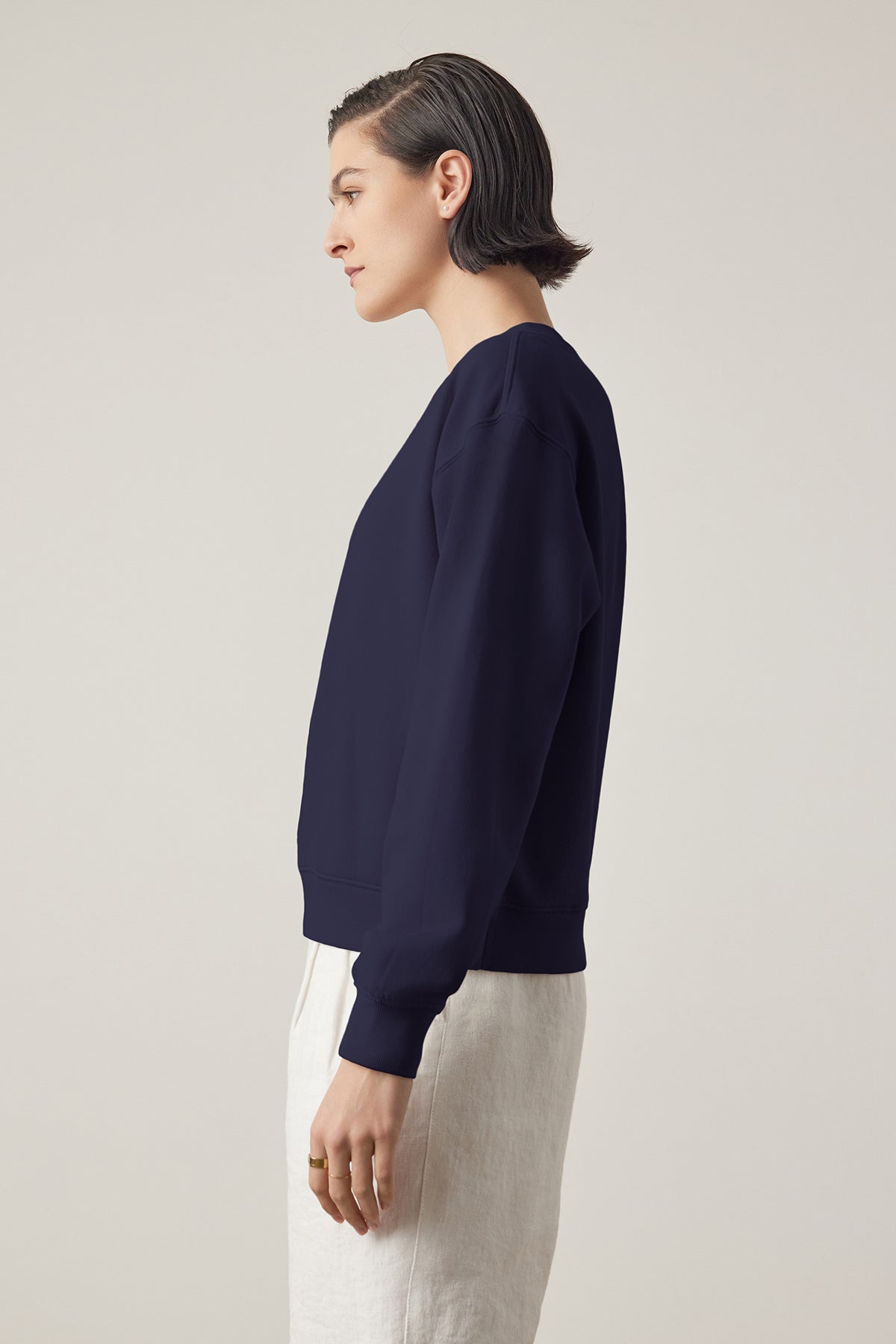 Side profile of a person with slicked-back hair wearing a Navy YNEZ SWEATSHIRT made by Velvet by Jenny Graham and light trousers against a neutral background.-36909403177153