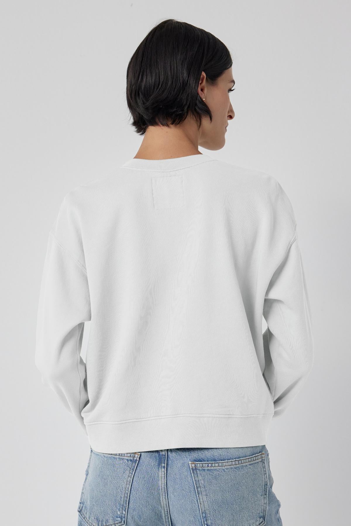 The back view of a woman wearing a white Velvet by Jenny Graham YNEZ SWEATSHIRT and jeans.-35678682218689
