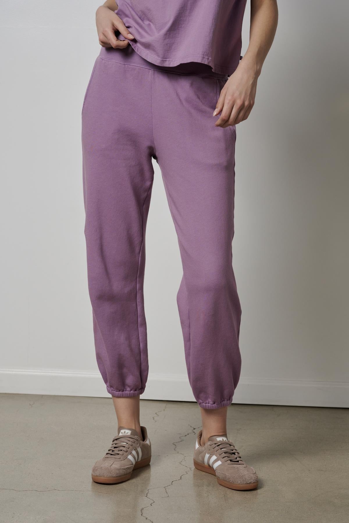   A woman wearing purple ZUMA sweatpants and sneakers. 