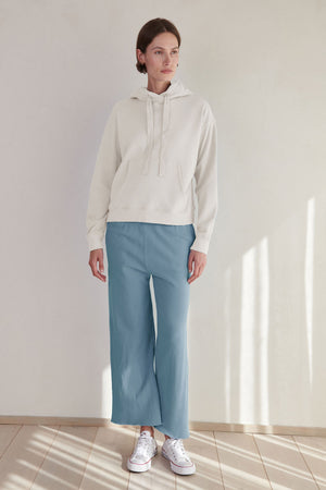 A woman wearing a white hoodie and blue Monetico sweatpant pants by Velvet by Jenny Graham.