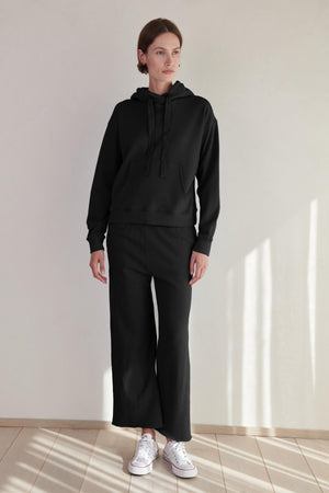 A woman wearing an OJAI HOODIE by Velvet by Jenny Graham and sweatpants.