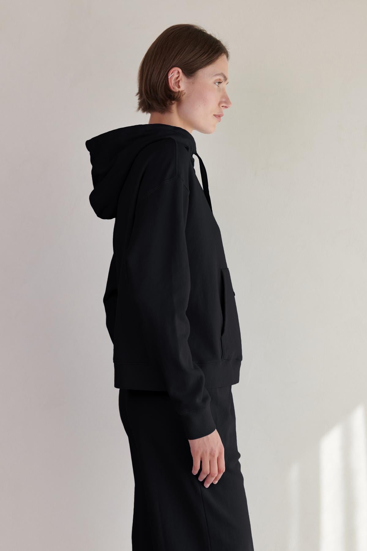   A woman wearing a black OJAI HOODIE and trousers by Velvet by Jenny Graham. 