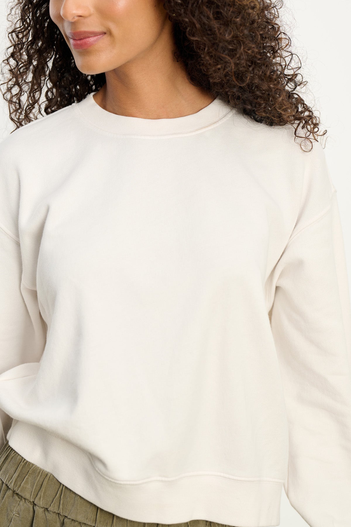 A woman wears the Velvet by Graham & Spencer YOKO SWEATSHIRT in plain off-white cotton fleece with olive green pants, shown from shoulders to waist against a neutral background.-40431120777409