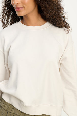A woman wears the Velvet by Graham & Spencer YOKO SWEATSHIRT in plain off-white cotton fleece with olive green pants, shown from shoulders to waist against a neutral background.