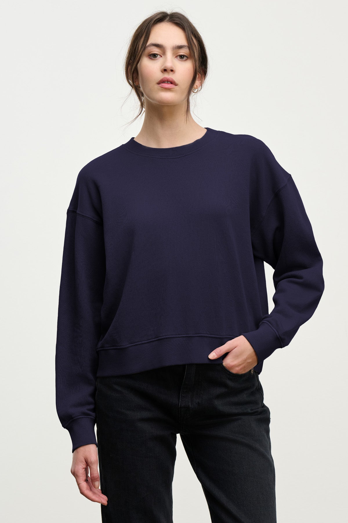 A person in a loose-fitting, long-sleeve YOKO SWEATSHIRT by Velvet by Graham & Spencer and black jeans poses against a plain light background, highlighting a relaxed silhouette.-40431164227777