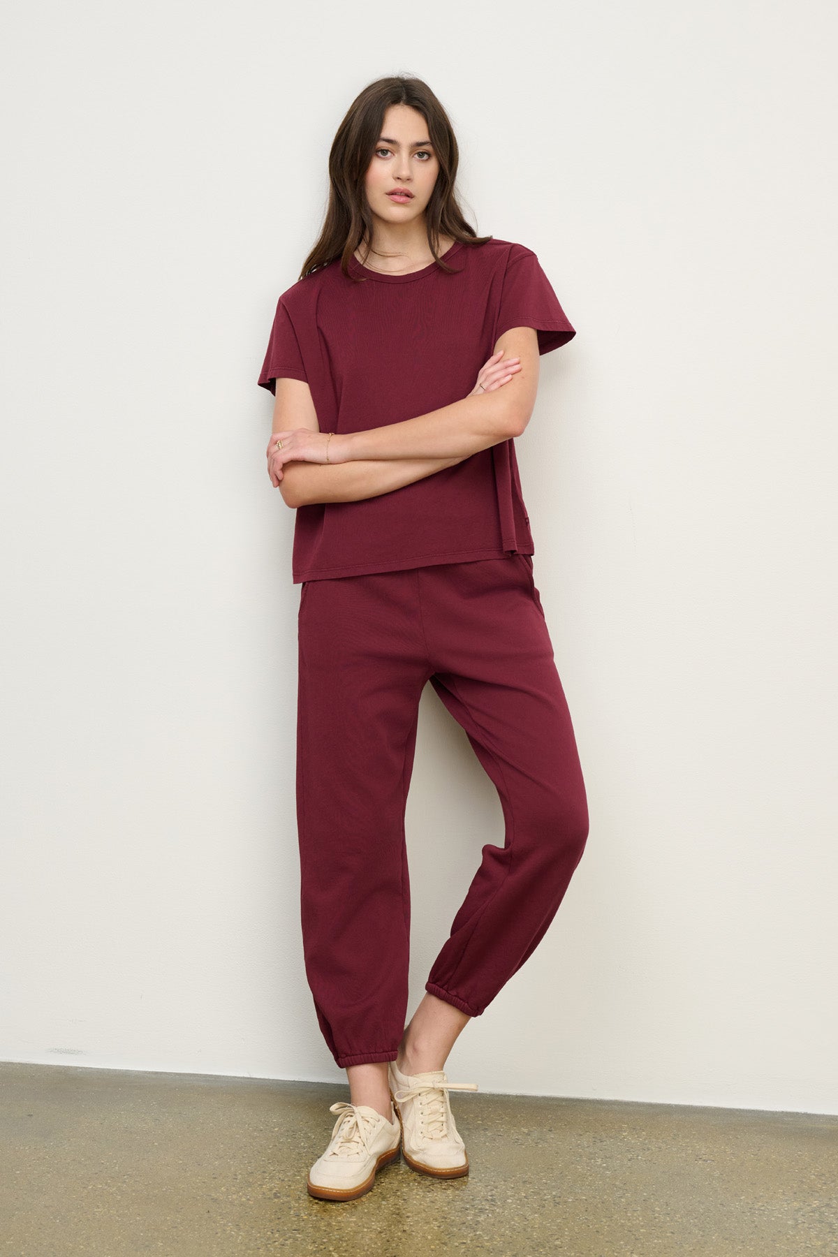 A woman stands against a plain wall wearing a relaxed fit burgundy short-sleeve top and Velvet by Graham & Spencer ZARA SWEATPANT joggers, paired with beige sneakers.-40328398635201