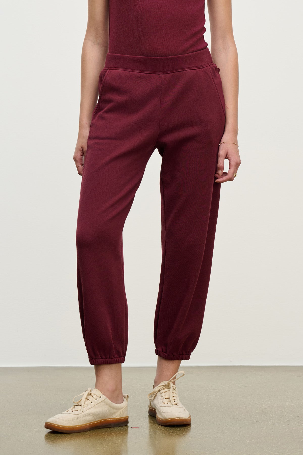 A person wearing Velvet by Graham & Spencer ZARA SWEATPANT in burgundy with relaxed fit and beige lace-up sneakers stands against a plain background.-40328398733505