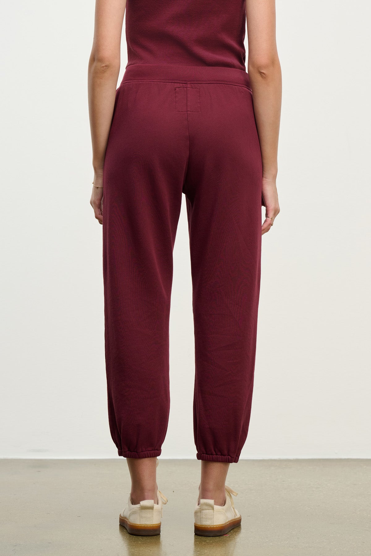 A person faces away, wearing Velvet by Graham & Spencer’s ZARA SWEATPANT joggers in a relaxed fit with maroon coloring and cream shoes, set against a plain background.-40328398799041