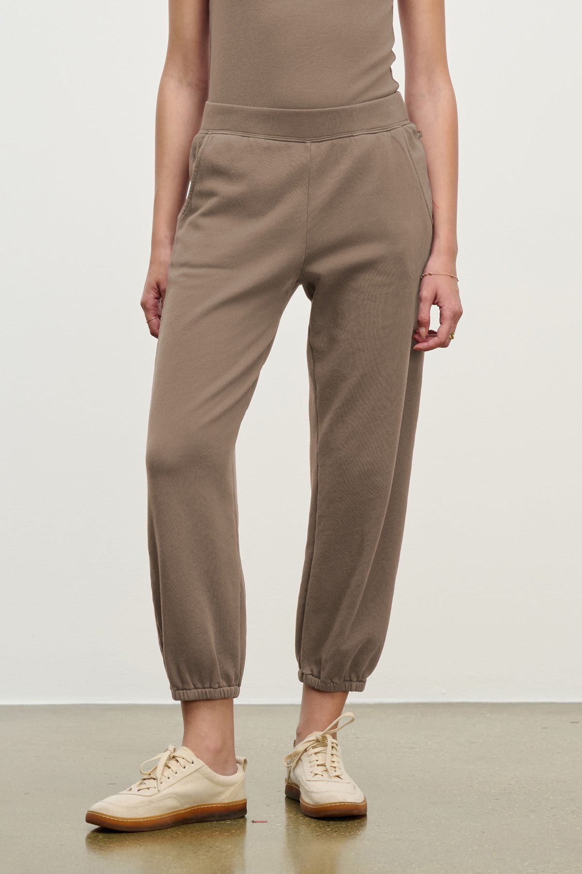 A person wears Velvet by Graham & Spencer’s ZARA SWEATPANT joggers in cotton fleece, featuring elastic cuffs and pockets, paired with beige sneakers, standing against a plain background.-40328398897345
