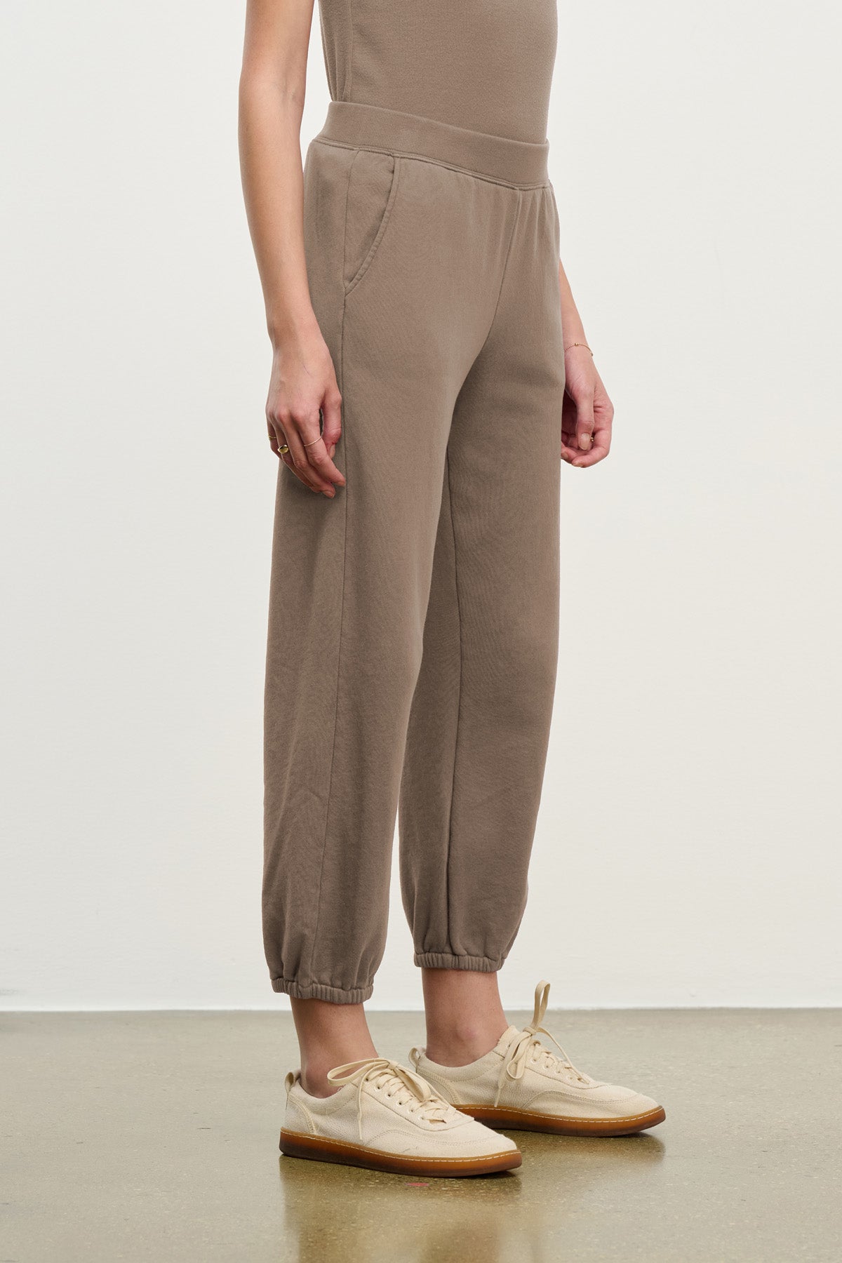 Someone stands against a plain background wearing Velvet by Graham & Spencer's ZARA SWEATPANT in a relaxed fit, paired with beige sneakers.-40328398930113