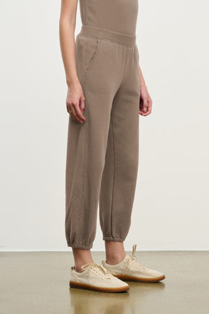 Someone stands against a plain background wearing Velvet by Graham & Spencer's ZARA SWEATPANT in a relaxed fit, paired with beige sneakers.