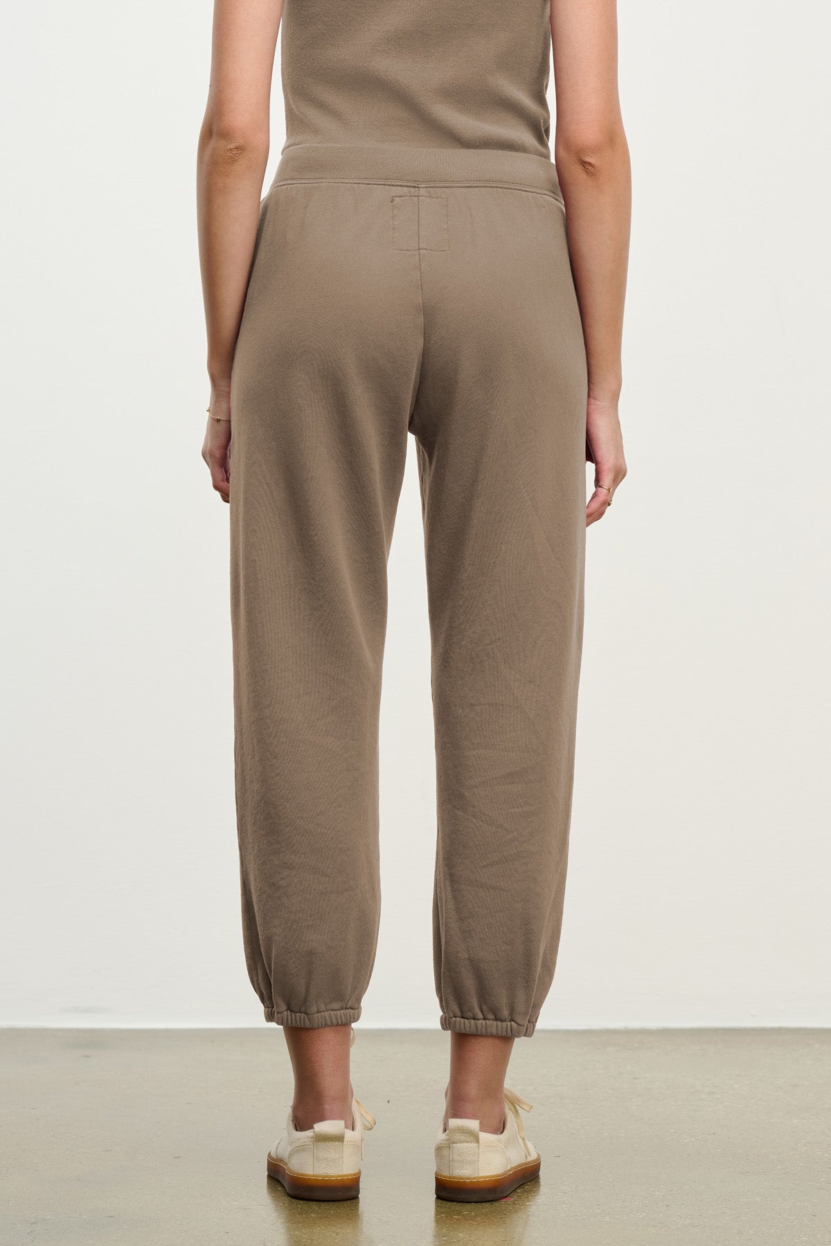 A person stands facing away, wearing Velvet by Graham & Spencer's ZARA SWEATPANT jogger in taupe cotton fleece with a matching top and beige shoes against a neutral background.-40328398962881
