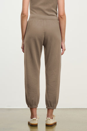 A person stands facing away, wearing Velvet by Graham & Spencer's ZARA SWEATPANT jogger in taupe cotton fleece with a matching top and beige shoes against a neutral background.