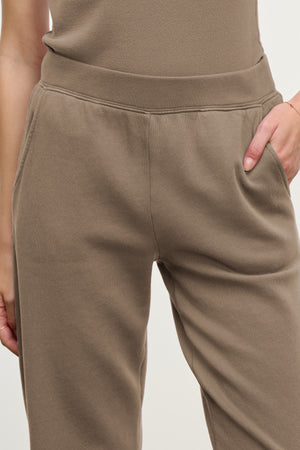 Model wearing Velvet by Graham & Spencer's ZARA SWEATPANT in taupe cotton fleece, relaxed fit, hands in pockets, photographed waist to thigh against a plain background.