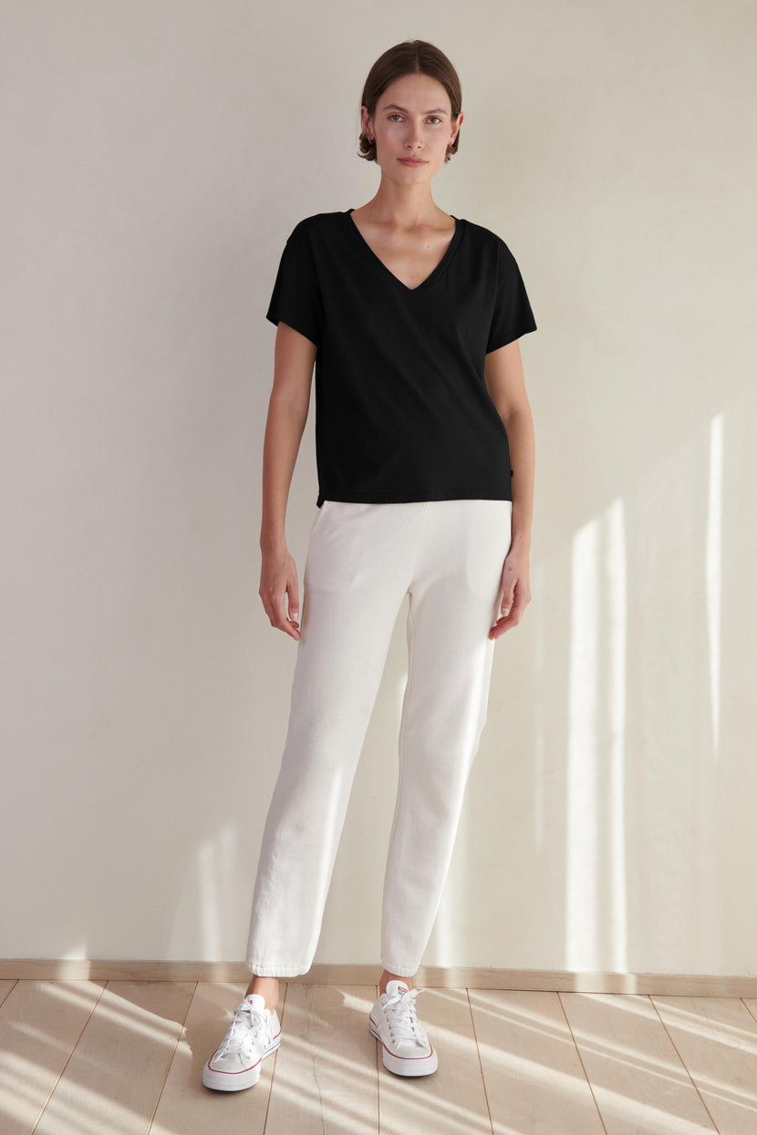 A woman wearing a black VENICE TEE by Velvet by Jenny Graham and white pants.