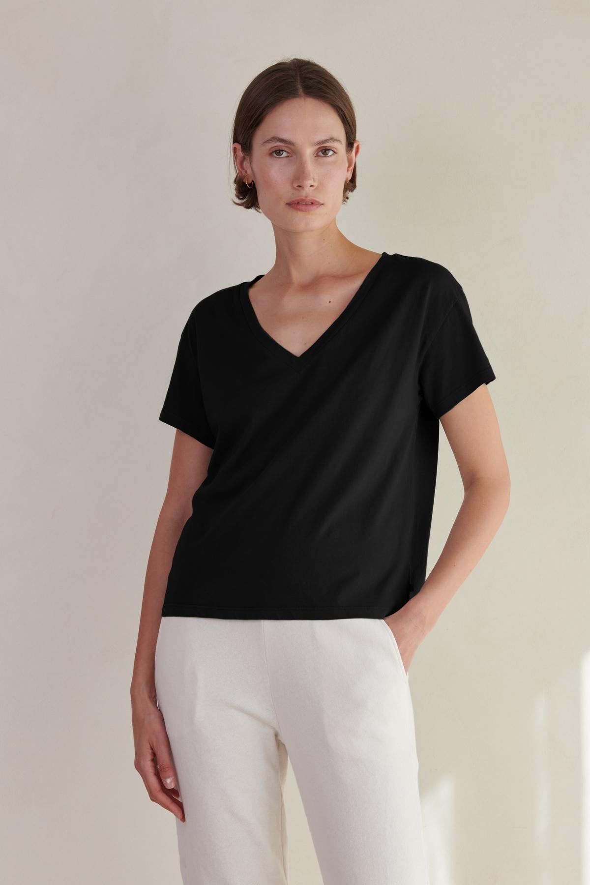 a woman wearing a black VENICE TEE by Velvet by Jenny Graham v - neck t - shirt and white pants.-26560813531329