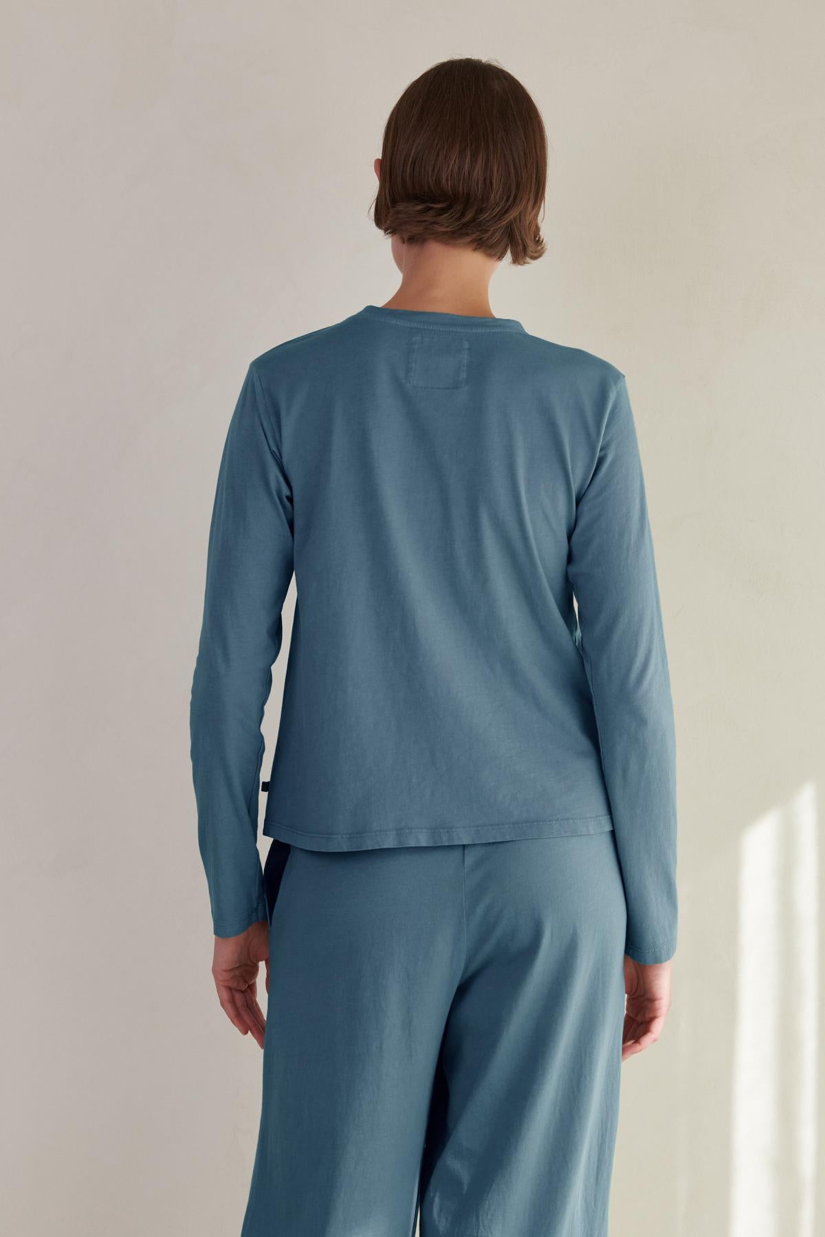  The woman is wearing a relaxed fit blue long-sleeved VICENTE TEE by Velvet by Jenny Graham and pants. 