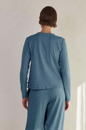 The woman is wearing a relaxed fit blue long-sleeved VICENTE TEE by Velvet by Jenny Graham and pants.