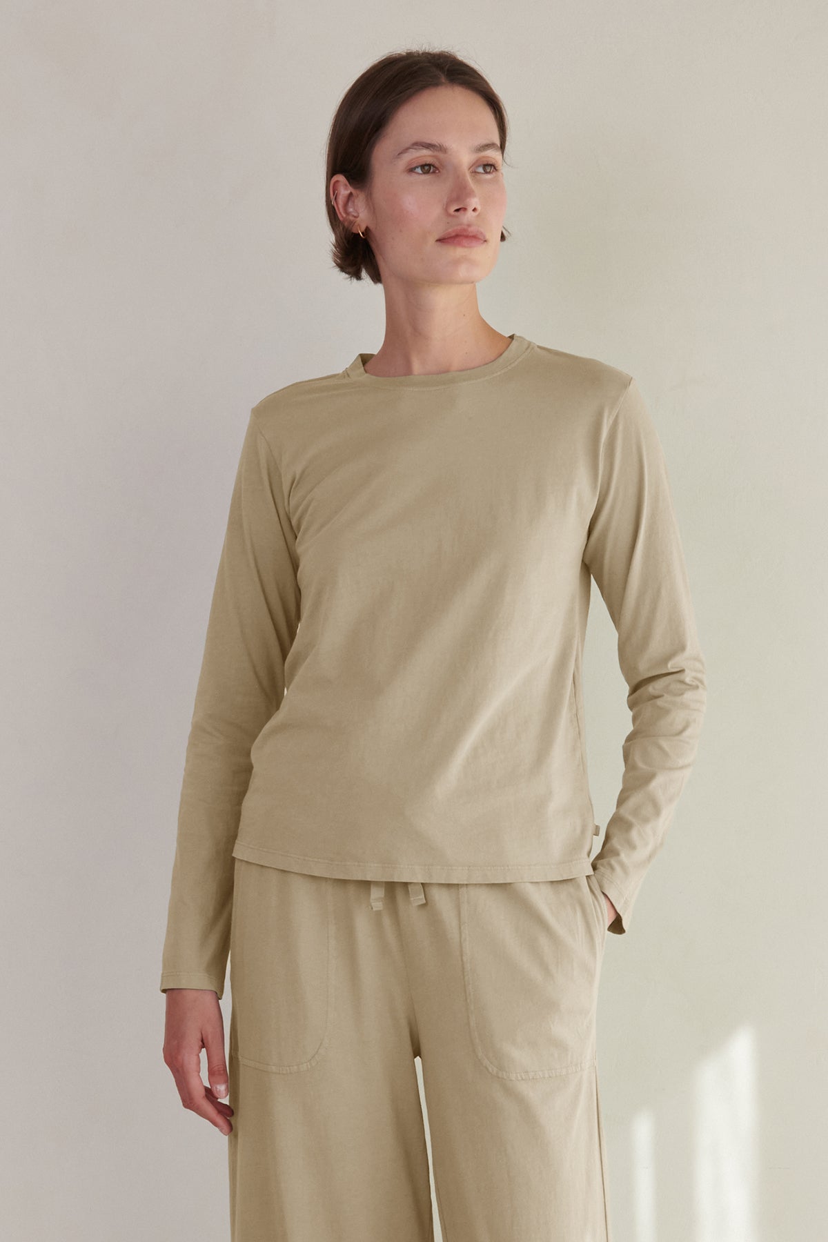 A woman wearing a beige long-sleeved VICENTE TEE and matching pants standing against a neutral background from Velvet by Jenny Graham.-36503755194561