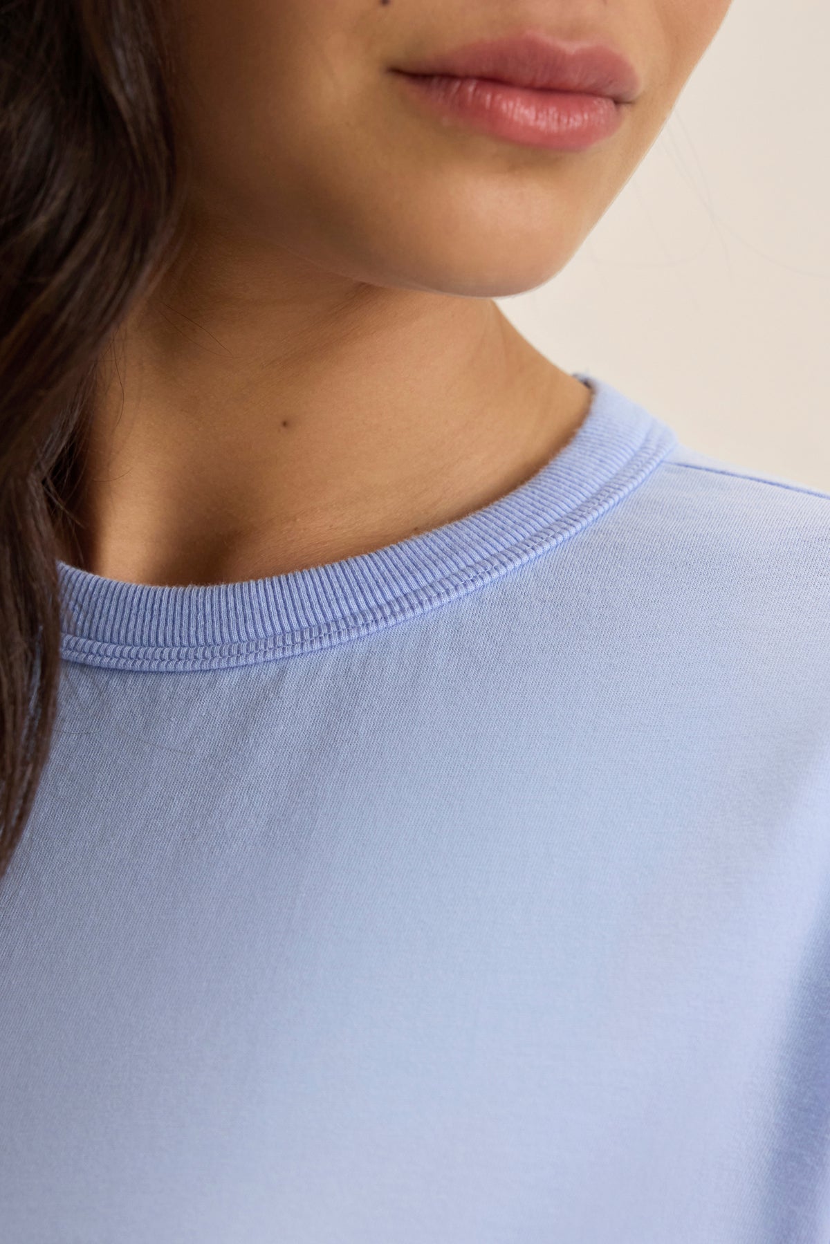   Close-up image of a person in the JAZZ TEE by Velvet by Graham & Spencer. The light blue shirt with a crew neckline highlights the individual's lip and chin details against a neutral background, showcasing its organic cotton jersey fabric with a relaxed boxy silhouette. 