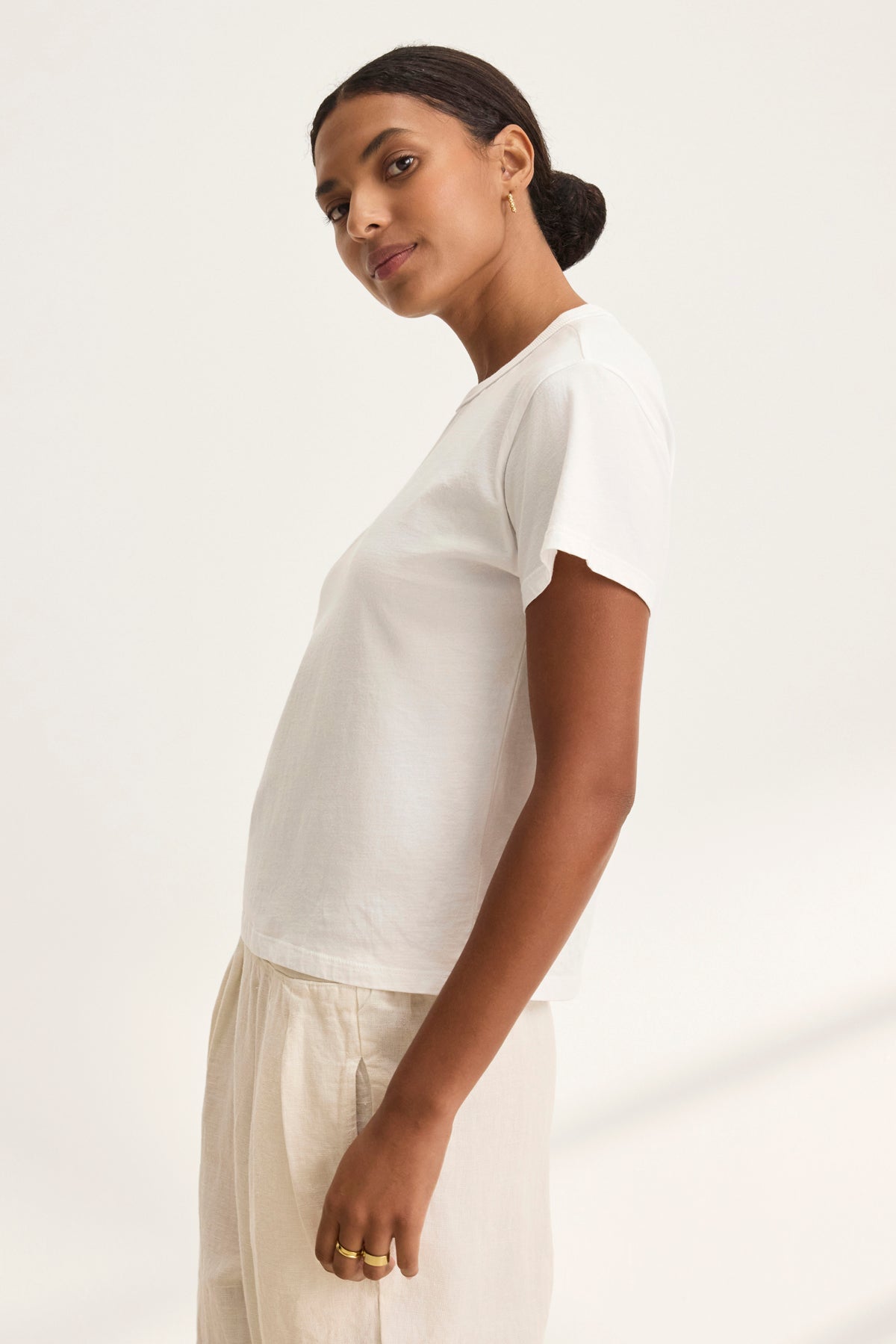 The individual is wearing a JAZZ TEE from Velvet by Graham & Spencer, featuring a relaxed boxy silhouette, paired with beige pants and standing sideways against a plain background.-38819698671809