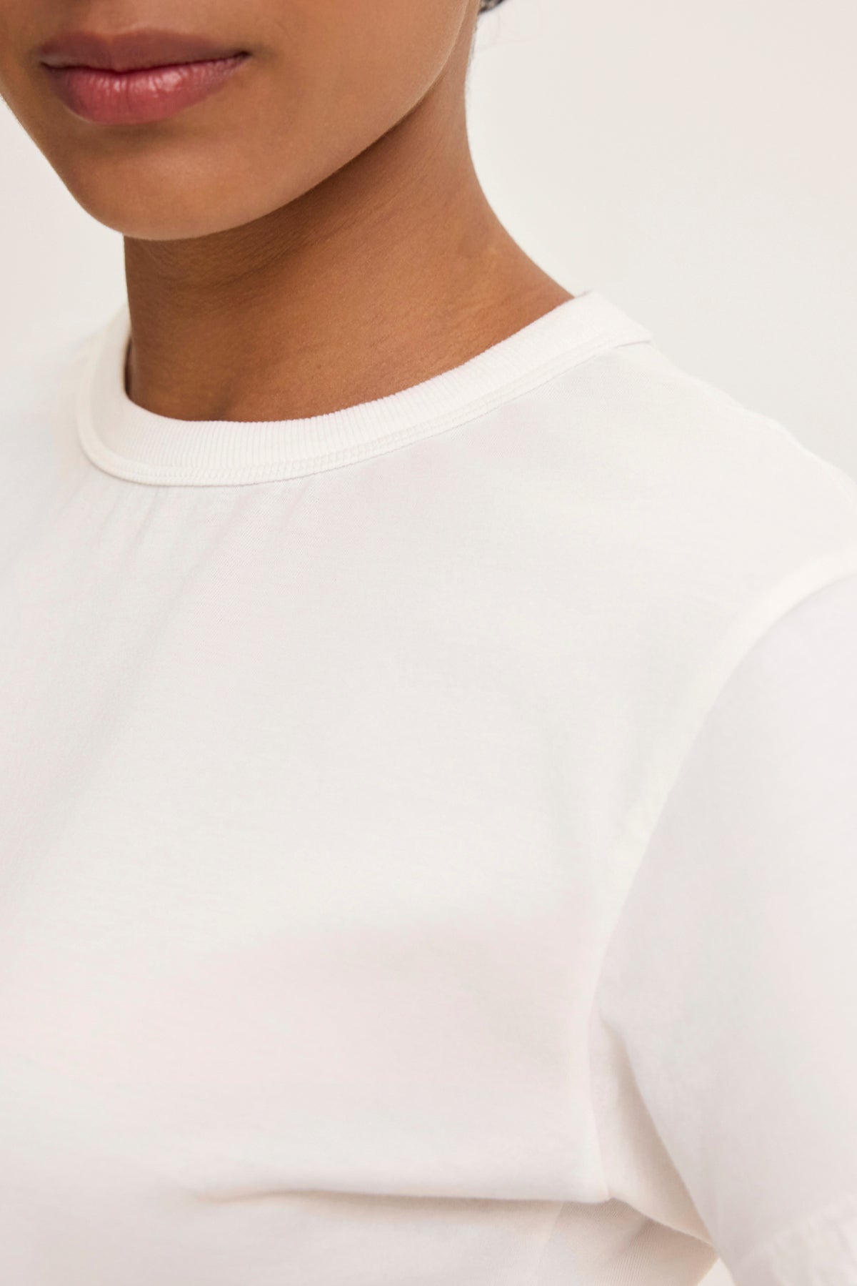   The individual is donning the JAZZ TEE from Velvet by Graham & Spencer, featuring a relaxed boxy silhouette in plain white, partially revealing their face and shoulder against a neutral background. 