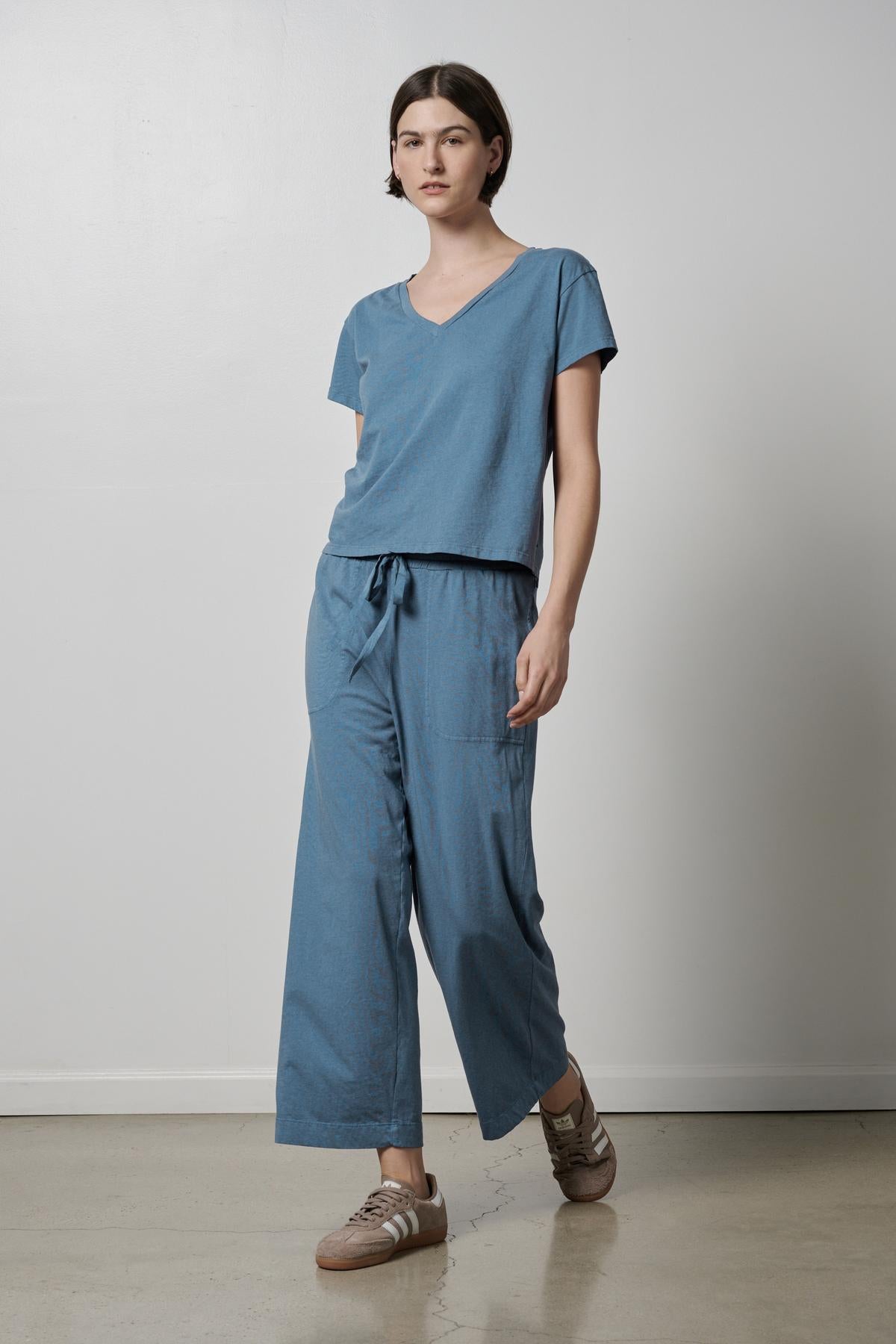   A woman wearing a Velvet by Jenny Graham organic cotton blue jumpsuit and sneakers with 90s silhouettes. 