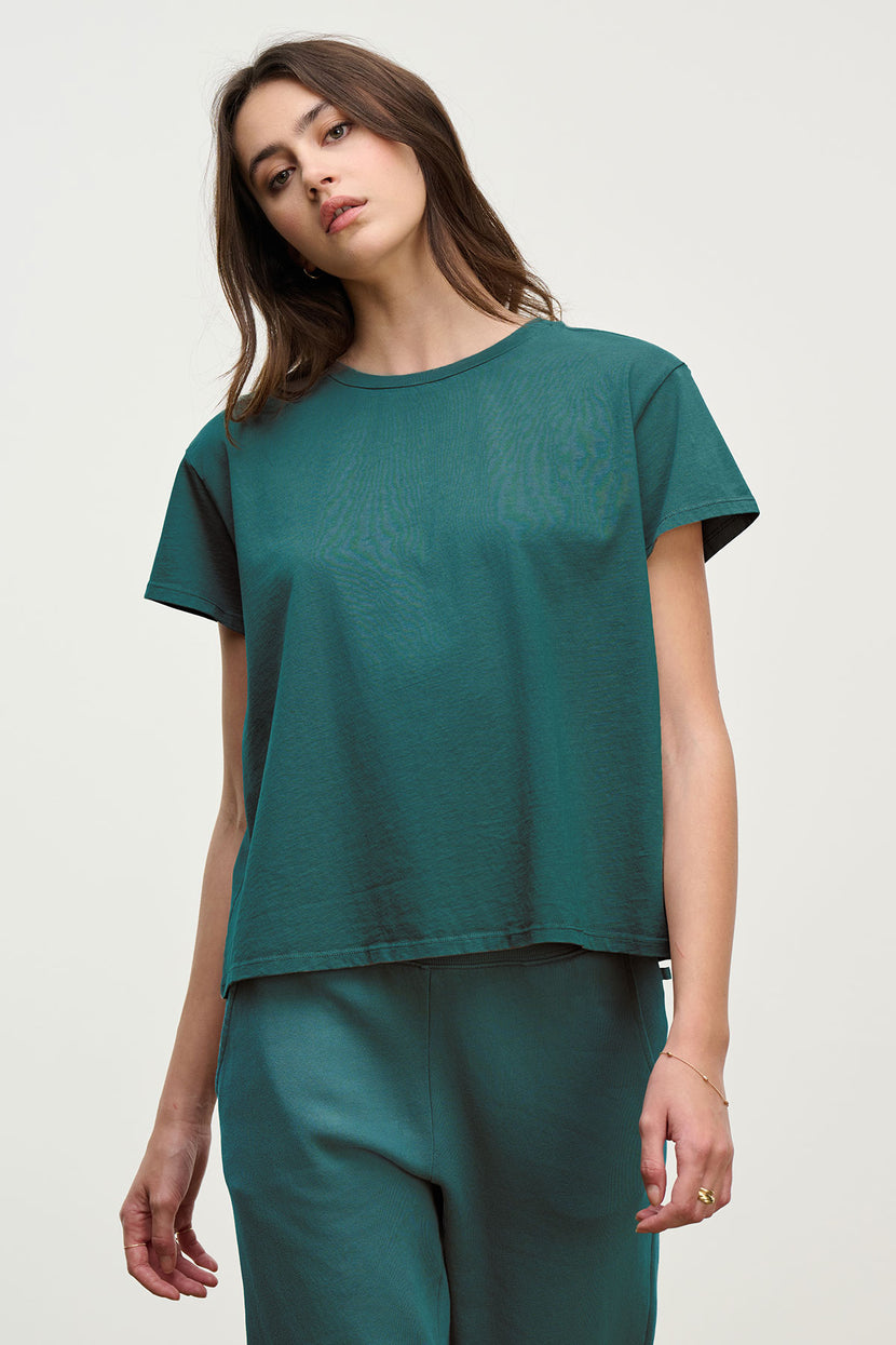 A woman wears the Velvet by Jenny Graham TOPANGA TEE, a relaxed-fit sustainable top, paired with matching green pants, standing against a plain light background.