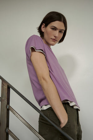 A woman in a purple Topanga Tee by Velvet by Jenny Graham leaning against a railing.