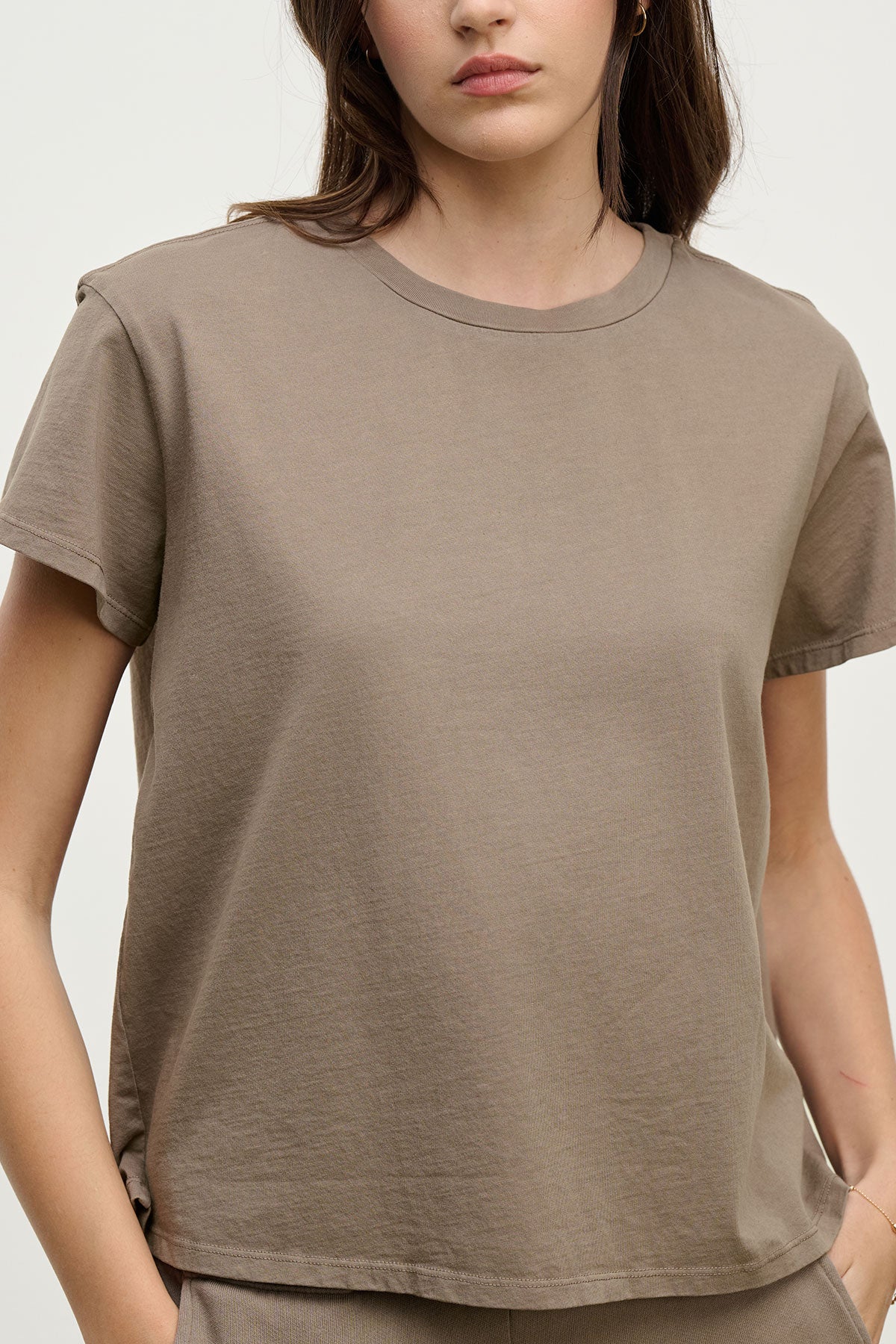 A woman wears the Velvet by Jenny Graham TOPANGA TEE in taupe—crafted from organic cotton with a relaxed fit—standing against a plain light background, ideal for easy transitions from work to workout.-39800471093441