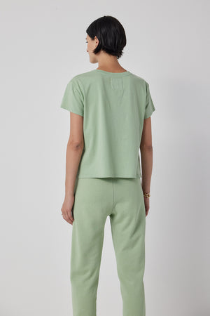 A person with short dark hair is shown from behind, wearing a light green short-sleeve shirt and Velvet by Jenny Graham's WESTLAKE SWEATPANT, which features an elastic drawstring waist. They are standing against a plain white background.