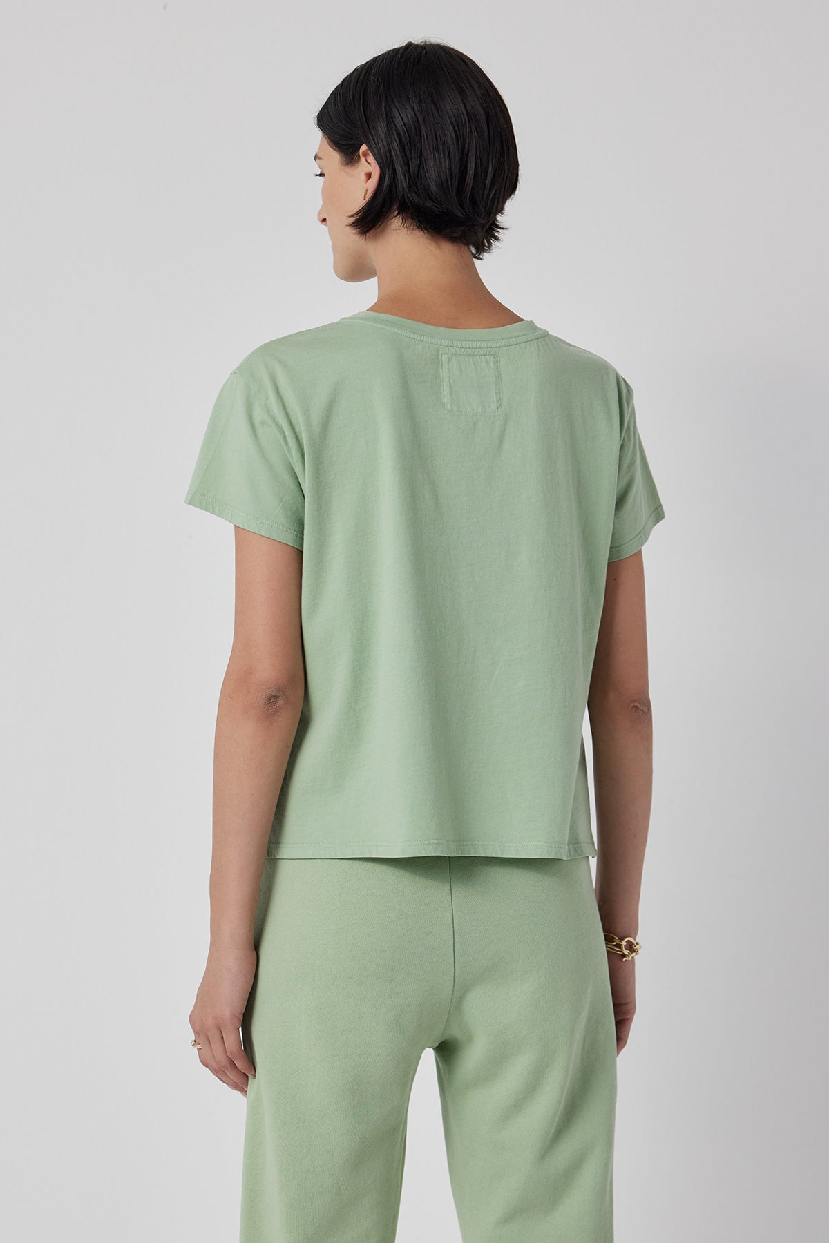   The back view of a woman wearing a green Velvet by Jenny Graham TOPANGA TEE and sweatpants. 