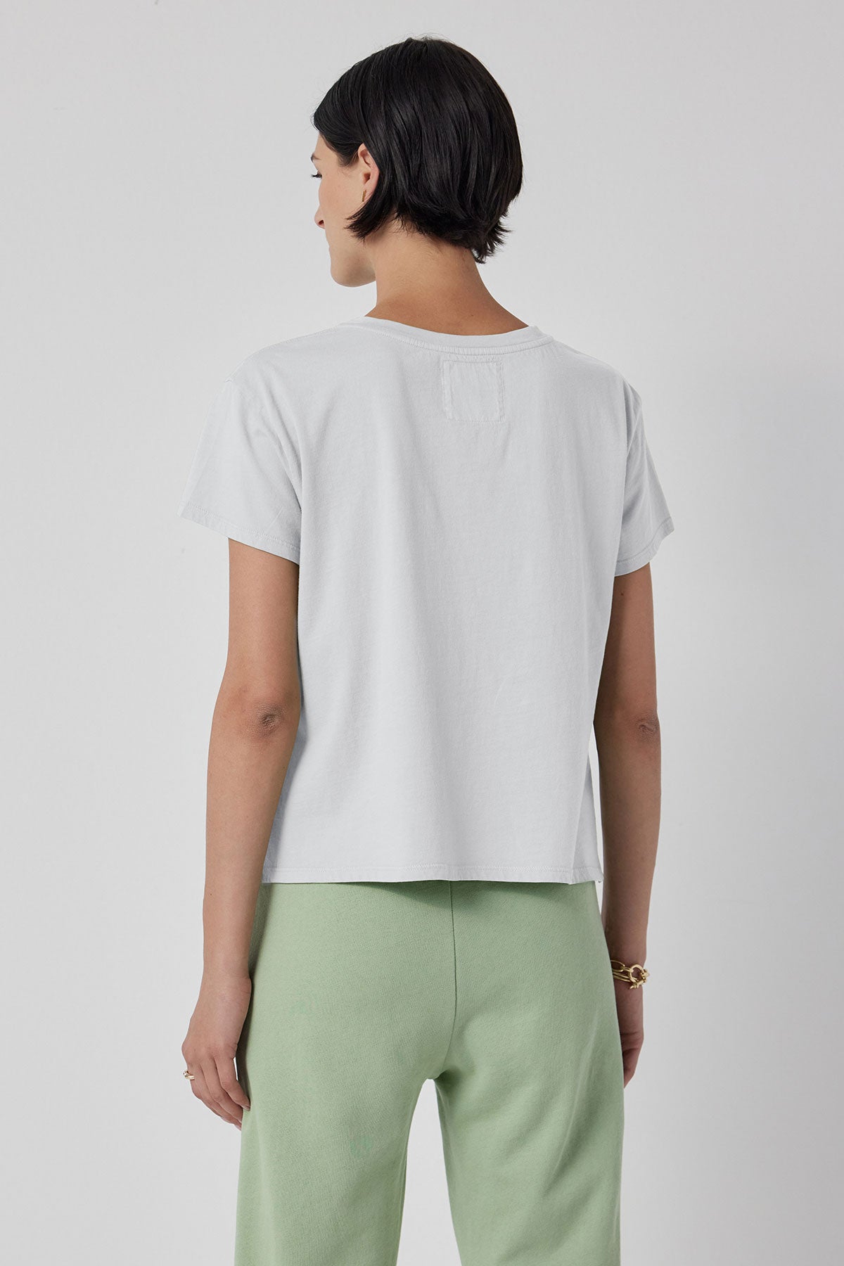 The back view of a woman wearing a white Velvet by Jenny Graham TOPANGA TEE and green sweatpants.-36212410581185