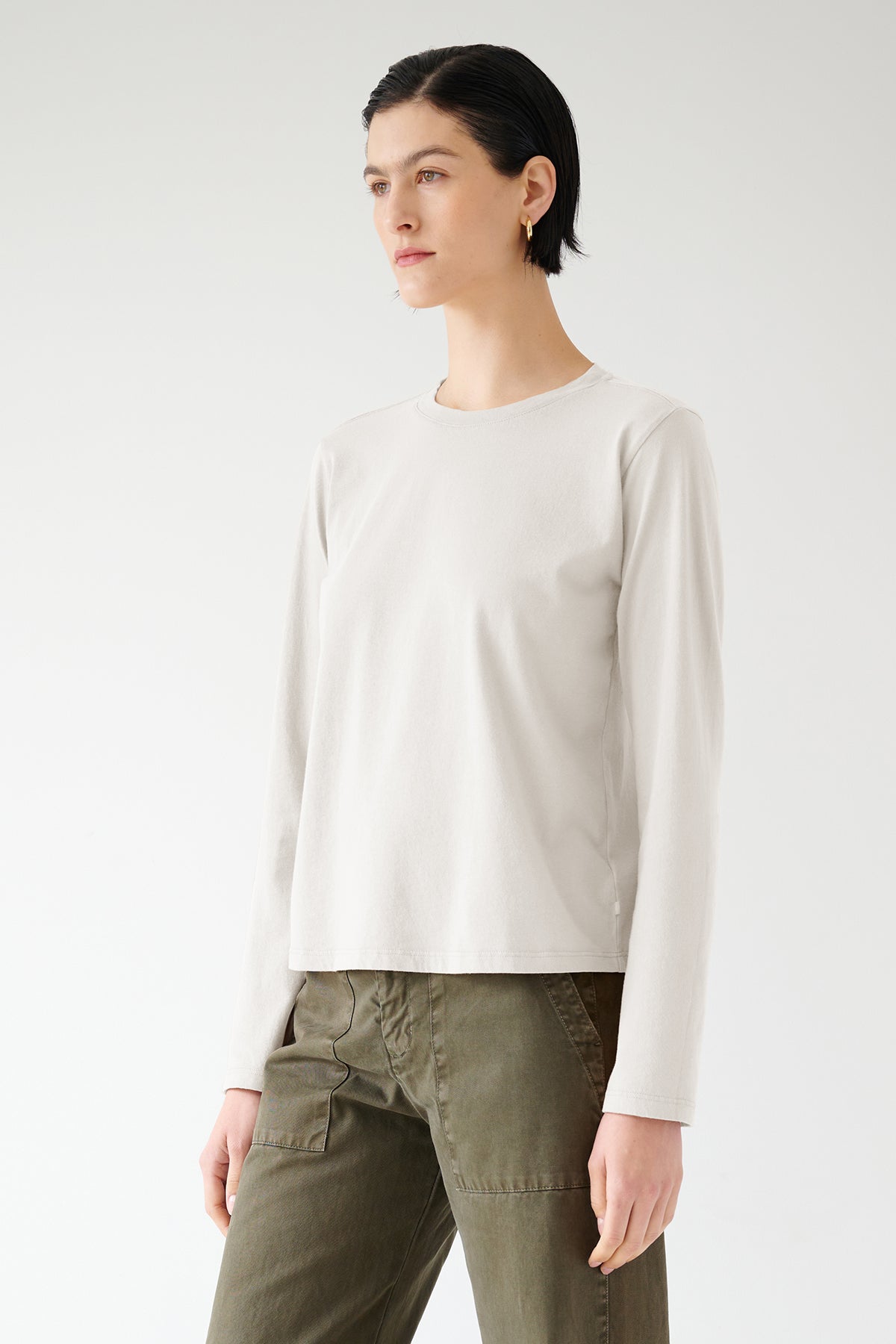 Woman in a Velvet by Jenny Graham VICENTE TEE and green pants standing against a light background.-36503793565889