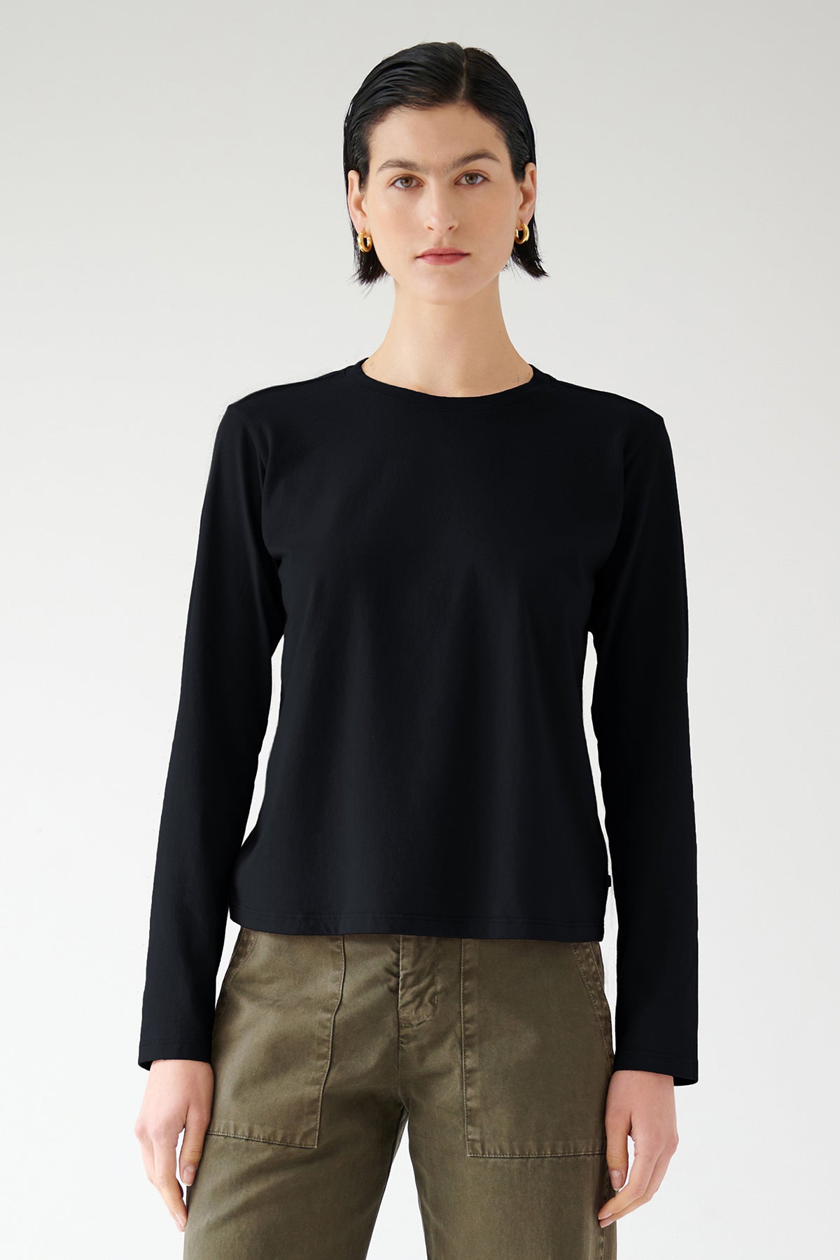 Woman wearing a black VICENTE TEE by Velvet by Jenny Graham and olive pants made of organic cotton, standing against a white background.-36503784095937