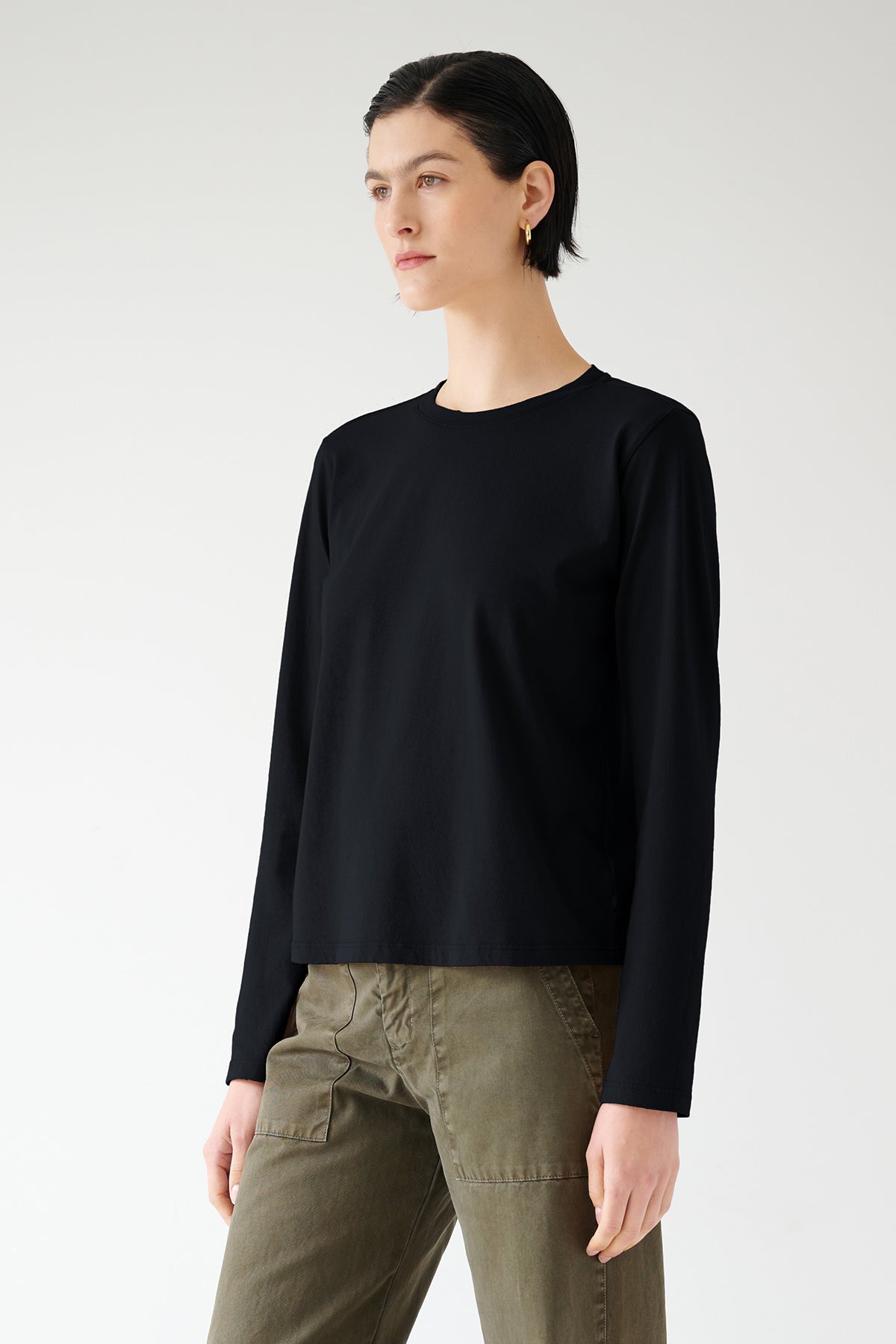   Woman posing in a seasonless Vicente Tee made of organic cotton by Velvet by Jenny Graham and olive green trousers against a white background. 