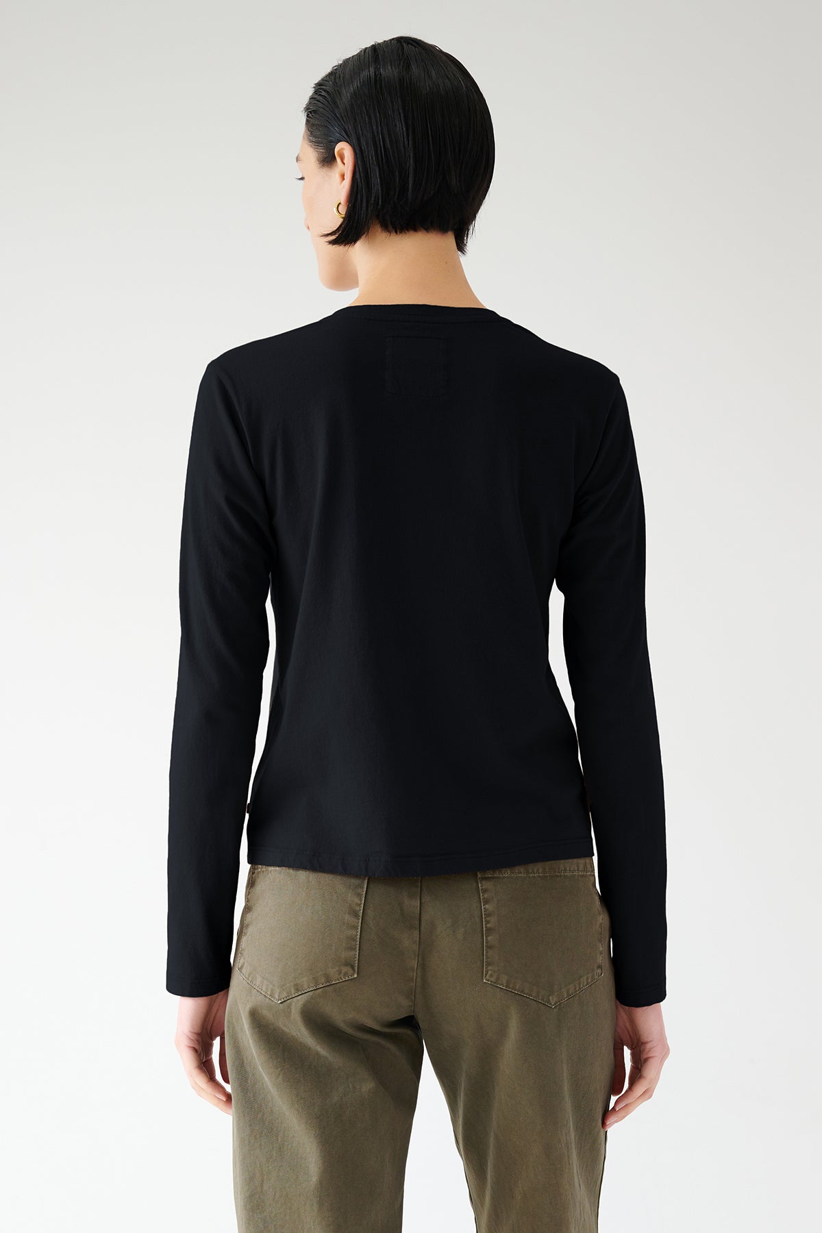   Woman wearing a Velvet by Jenny Graham VICENTE TEE in black and olive pants seen from the back. 