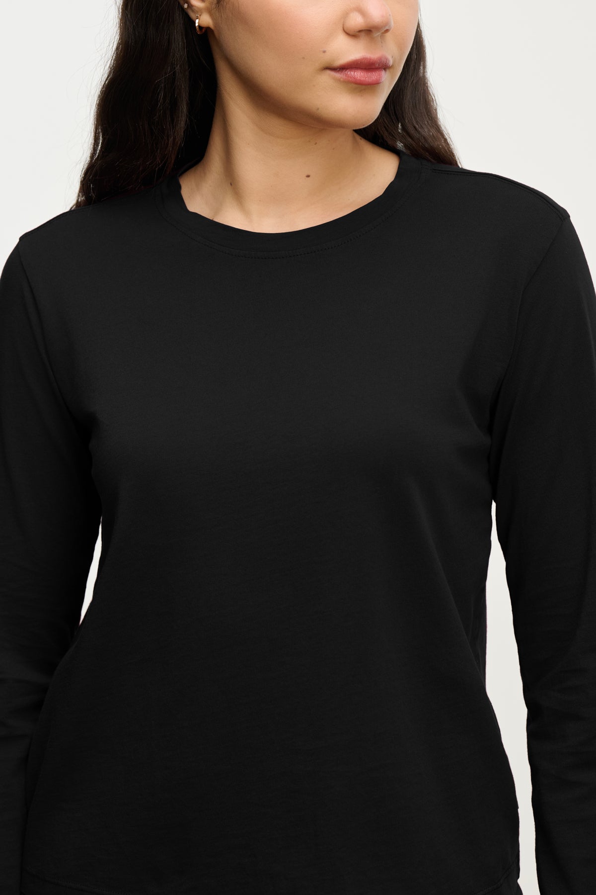 A woman wears the VICENTE TEE by Velvet by Jenny Graham, a relaxed-fit, plain black organic cotton long sleeve shirt, shown from shoulders to waist and facing slightly right for an effortless look.-39800065360065