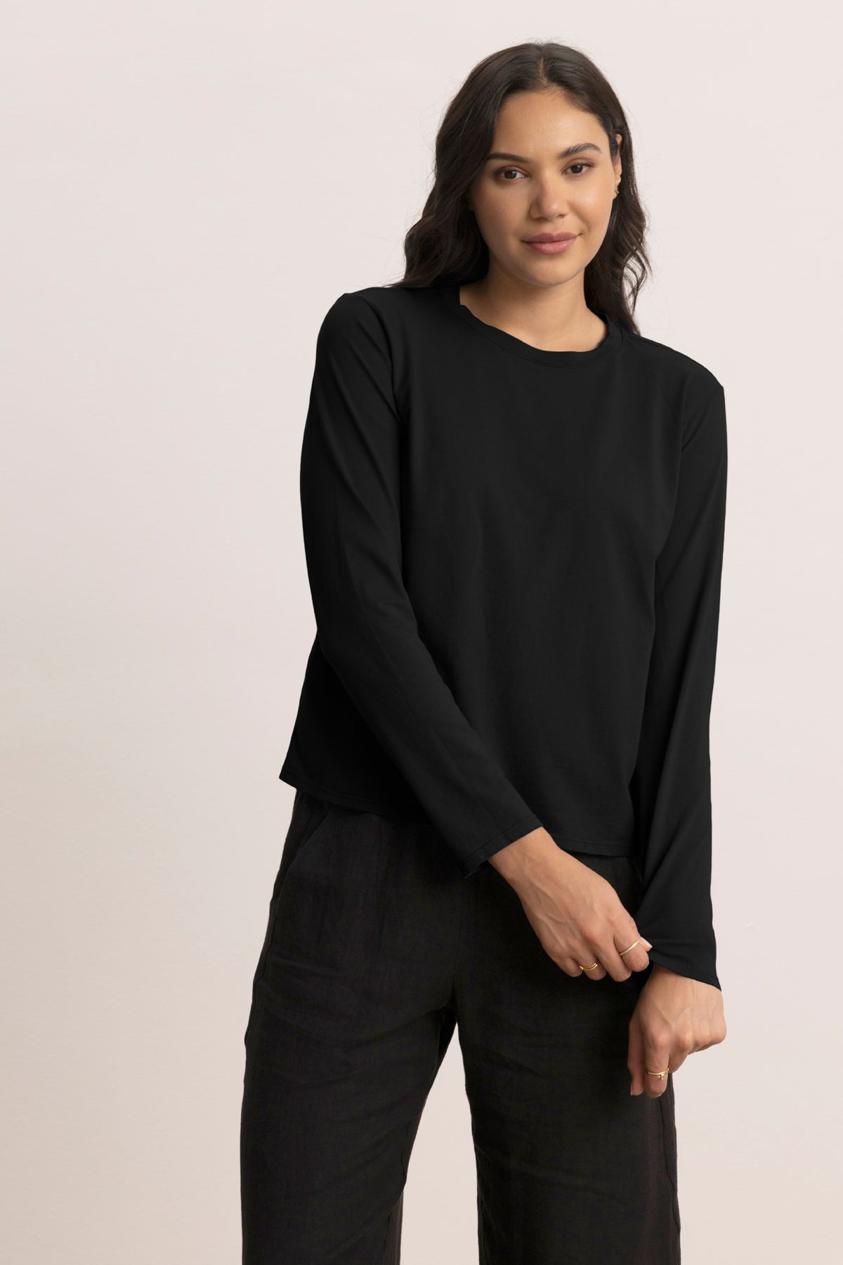 A woman poses against a light background wearing the relaxed fit VICENTE TEE by Velvet by Jenny Graham and black pants, with one arm bent as she holds her other wrist.-39800065327297