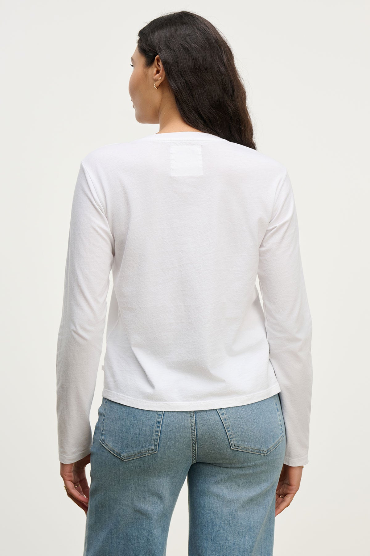 A woman with long dark hair is shown from the back wearing the Velvet by Jenny Graham VICENTE TEE, a relaxed fit organic cotton long sleeve shirt, paired with light blue jeans against a plain light background.-39800486789313
