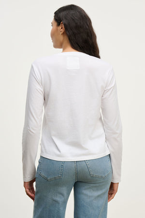 A woman with long dark hair is shown from the back wearing the Velvet by Jenny Graham VICENTE TEE, a relaxed fit organic cotton long sleeve shirt, paired with light blue jeans against a plain light background.