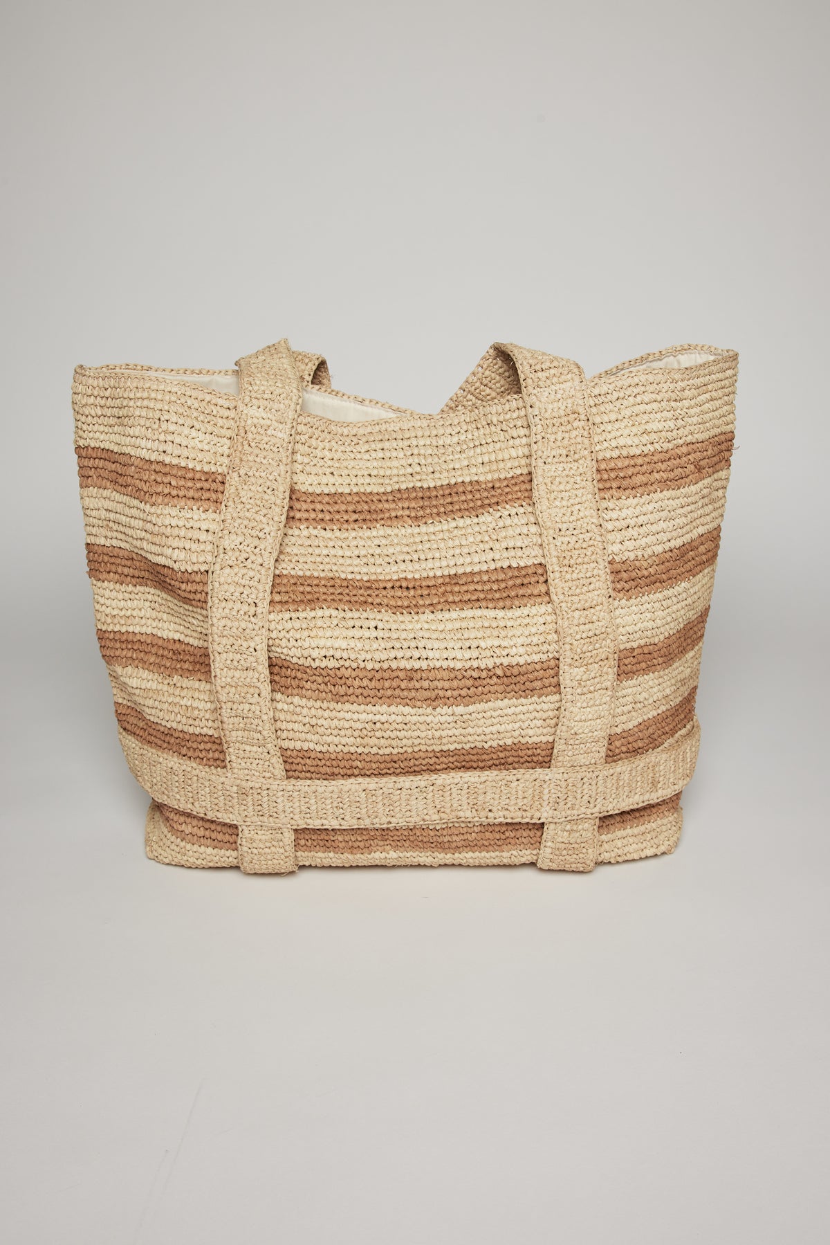   A striped raffia straw tote bag with beige and white horizontal stripes, featuring sturdy handles, displayed against a neutral background. 
Product Name: The Original Straw Traveler Bag
Brand Name: Velvet by Graham & Spencer 