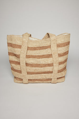 A striped raffia straw tote bag with beige and white horizontal stripes, featuring sturdy handles, displayed against a neutral background. 
Product Name: The Original Straw Traveler Bag
Brand Name: Velvet by Graham & Spencer