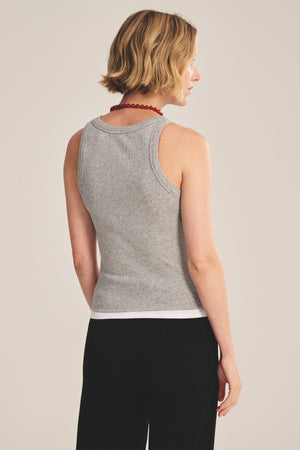 A person with short blond hair is shown from the back, wearing the ORION TANK TOP by Velvet by Graham & Spencer in gray, paired with black pants and a red bead necklace against a plain background.