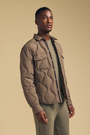 A man stands against a beige background wearing the DANILO QUILTED JACKET by Velvet by Graham & Spencer over a green shirt and matching pants, exemplifying refined men’s outerwear.