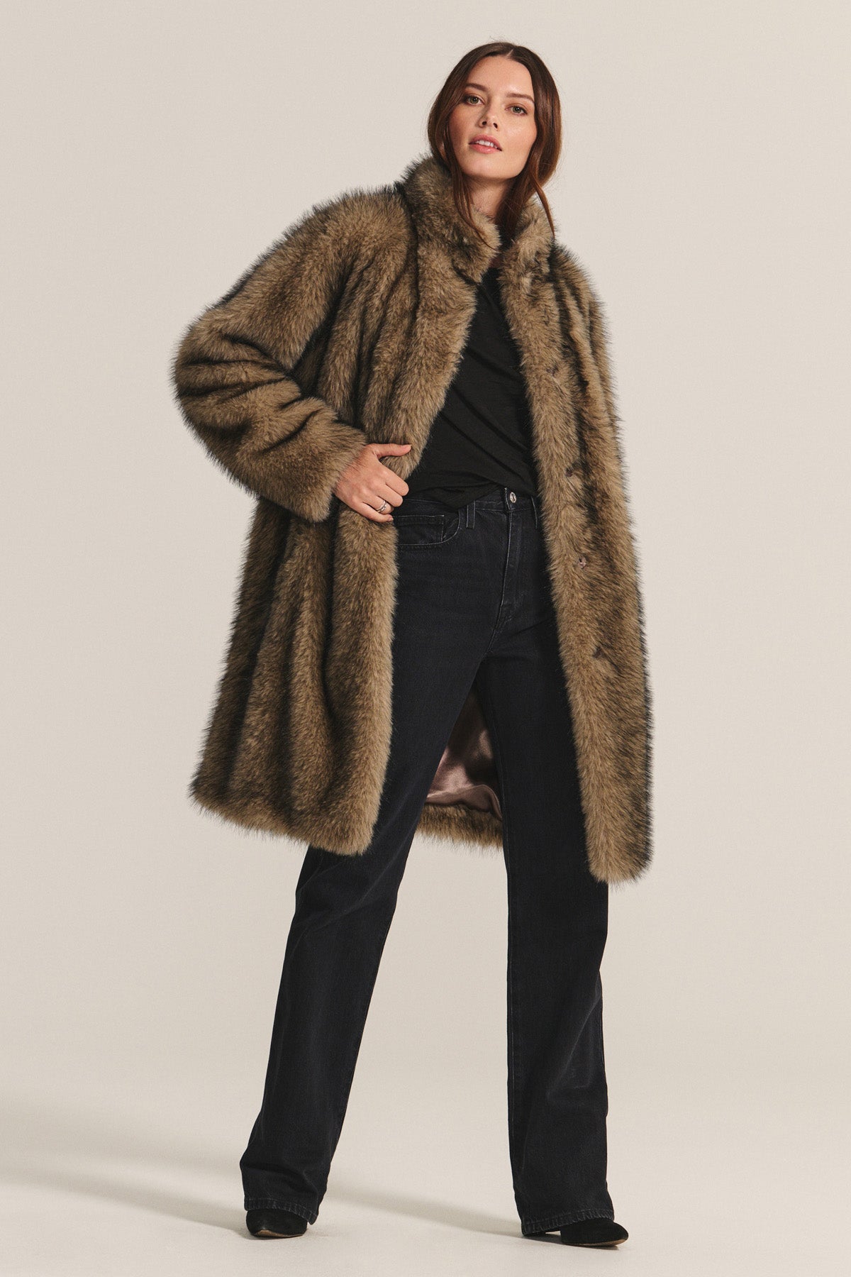 A person models the ADALYNN LUXE FAUX FUR JACKET by Velvet by Graham & Spencer—a long brown faux fur coat with a detachable faux leather belt—styled over a black top and dark jeans, perfect for chic cold-weather looks.-40263642022081