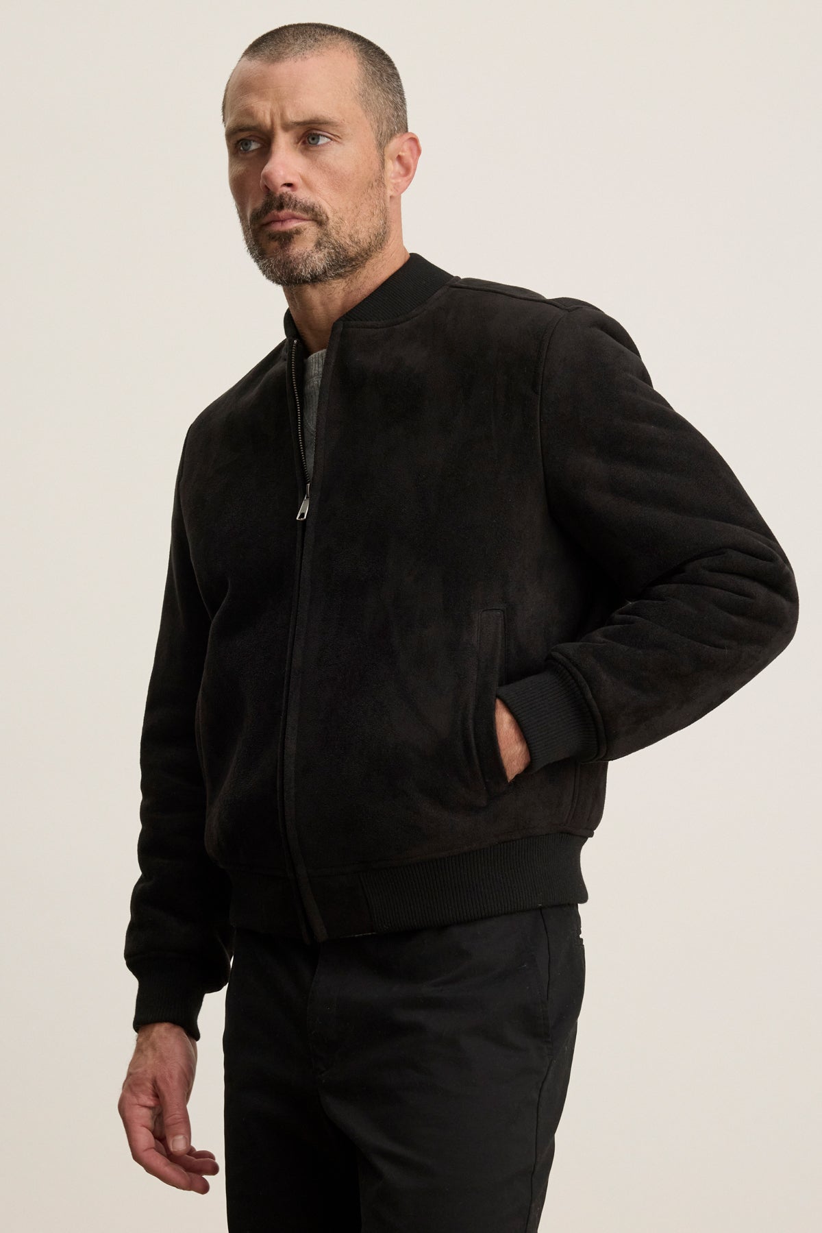 A man with a short beard and close-cropped hair wears the AMIAS BOMBER JACKET by Velvet by Graham & Spencer with black pants, standing against a plain light background.